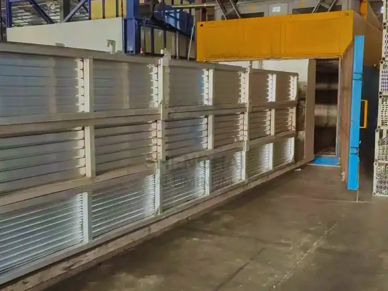 Perfiles de extrusión de aluminio cargados en bastidores que entran en el horno de envejecimiento industrial para su tratamiento térmico.