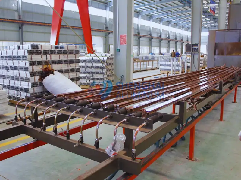 Perfiles de aluminio en la línea de producción de impresión por transferencia de vetas de madera en una planta de fabricación.
