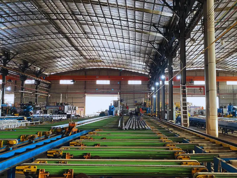 Descripción general de un gran taller industrial con rodillos transportadores verdes para la fabricación de extrusiones de aluminio.