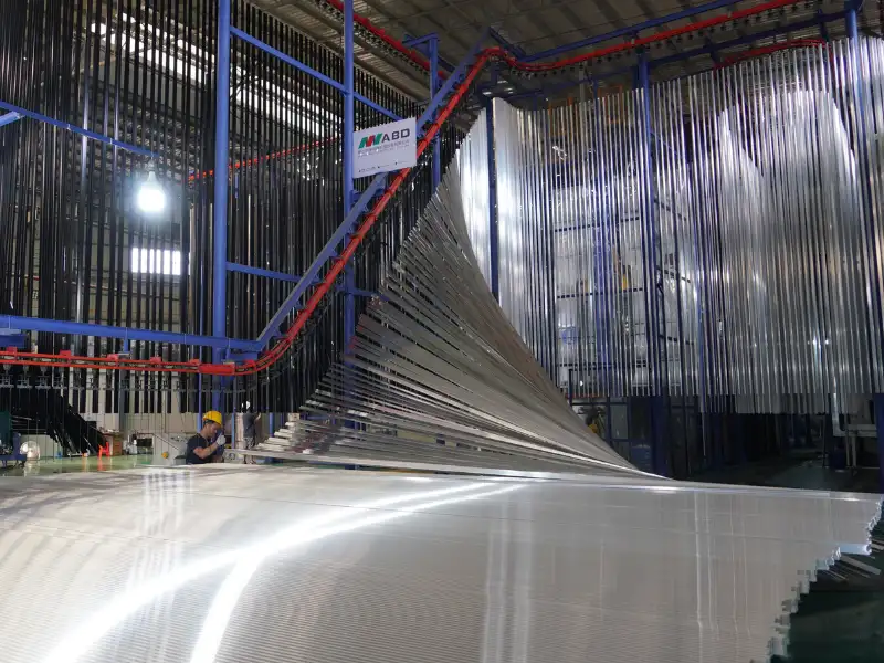 Trabajadores operando una línea vertical de recubrimiento en polvo y anodizado para perfiles de aluminio en una fábrica.